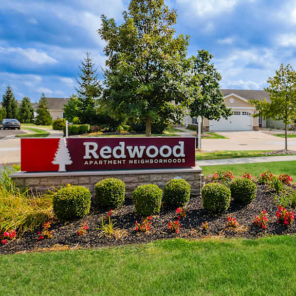 a sign for redwood apartment neighborhoods is in the foreground of a well-kept lawn.