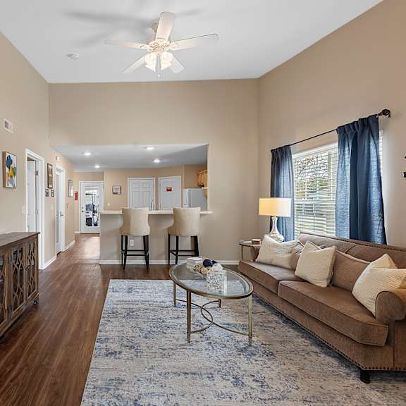 a living room with a brown couch, a glass coffee table, and a ceiling fan.