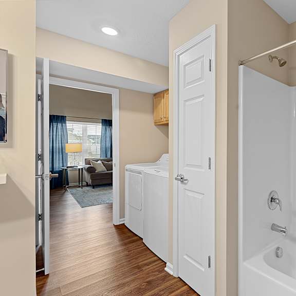 a white bathroom with a tub and a door leading to a living room.