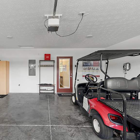 a red golf cart is parked in a large, empty room with a wooden door and a red fire extinguisher on the wall.