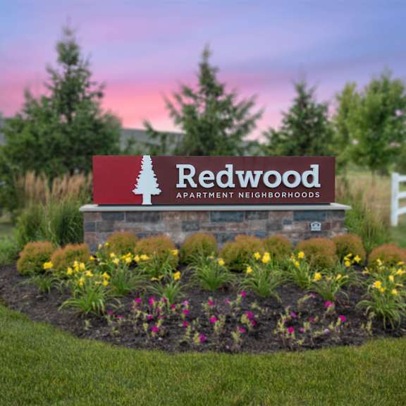 a sign for redwood apartment neighborhoods is surrounded by flowers and greenery.