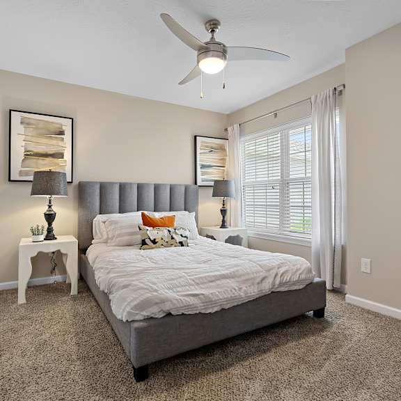 a bedroom with a bed, a ceiling fan, and a small table with a lamp on it.