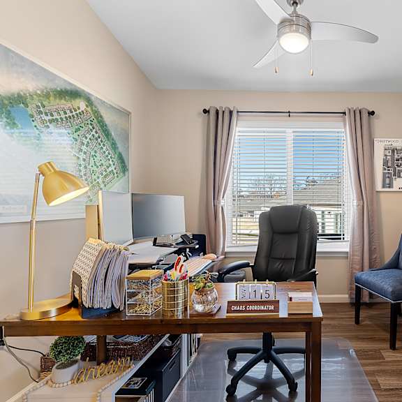a room with a desk, chairs, and a fan.