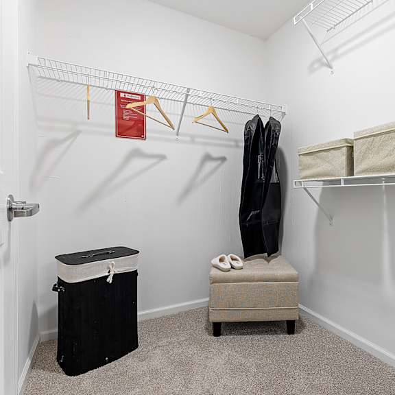 a small room with a white door, a black bin, a black coat, a bench, and a coat rack.