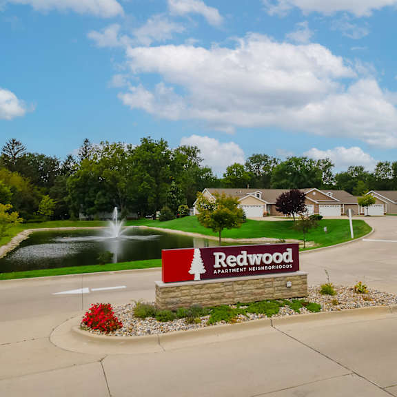 a sign for redwood apartment neighborhood sits in front of a pond and houses.