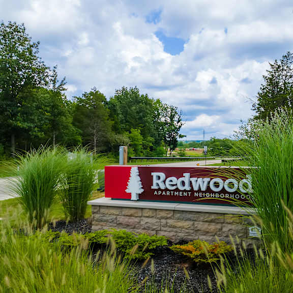 a sign for redwood apartment neighborhood sits in front of a grassy area.