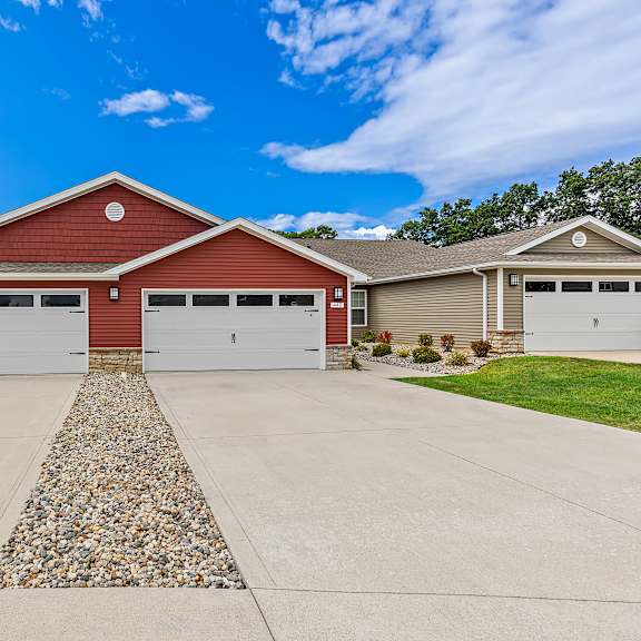 a two-car garage with a red roof and white doors is surrounded by a gravel driveway.