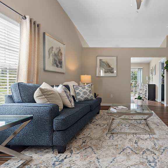 a living room with a grey couch, a glass coffee table, and a flat screen tv mounted on the wall.