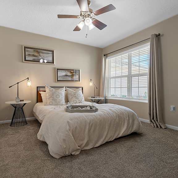 a bedroom with a bed, a ceiling fan, and a window with curtains.
