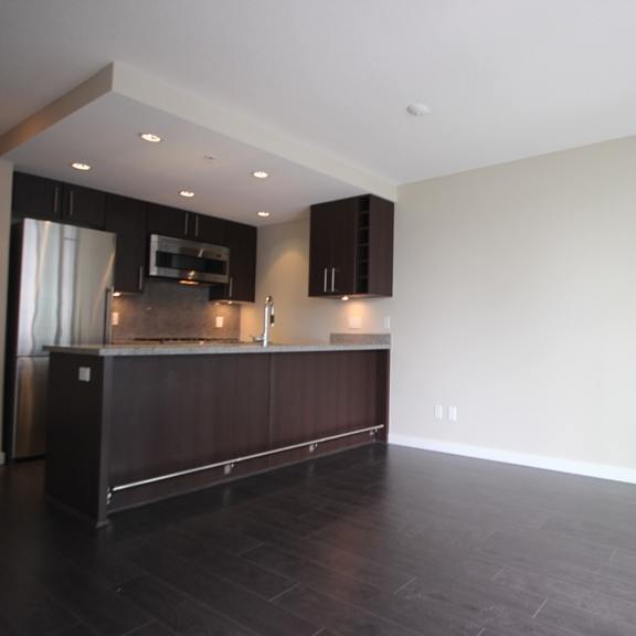 an empty living room with a large window and a kitchen in the background