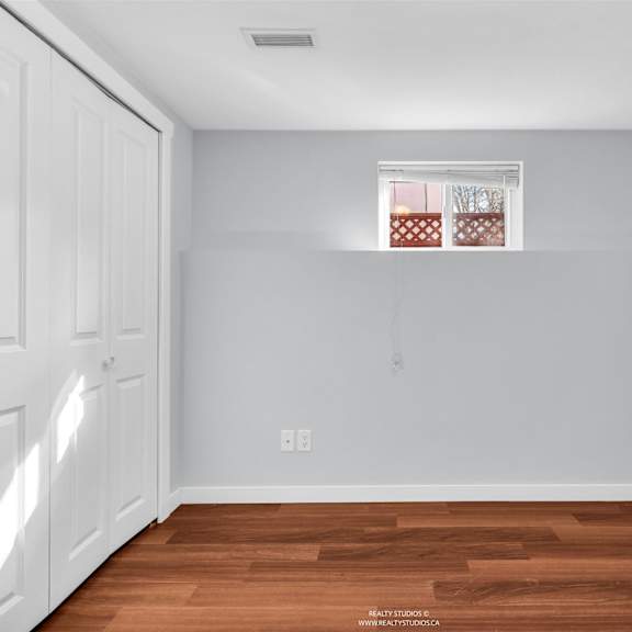 a room with white walls and wooden flooring with a window.