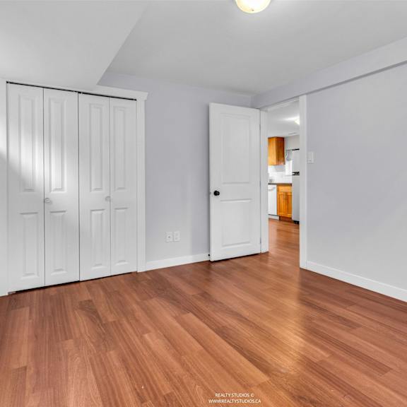 a room with white walls and wooden flooring, featuring a white door and a set of white cabinets.