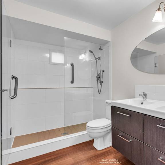a modern bathroom with a white sink, toilet, and a walk-in shower.