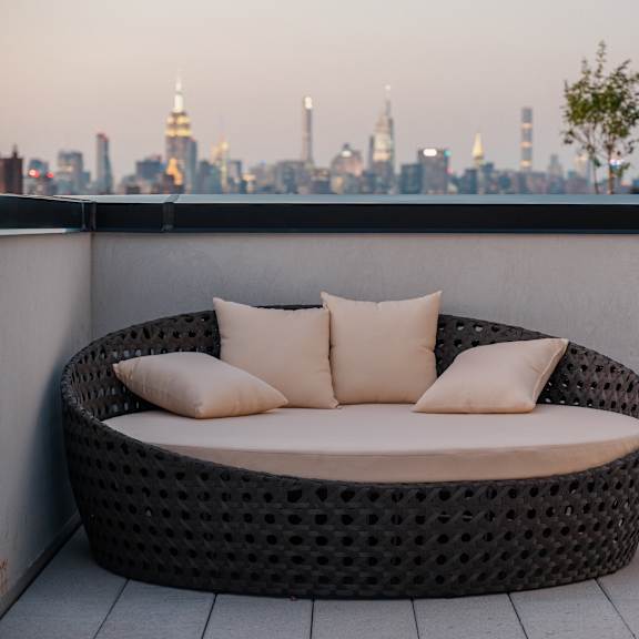 a round rattan sofa with pillows on a balcony overlooking a city
