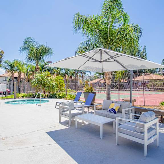 a patio with two lounge chairs and an umbrella with a pool in the background at metro 3610, california