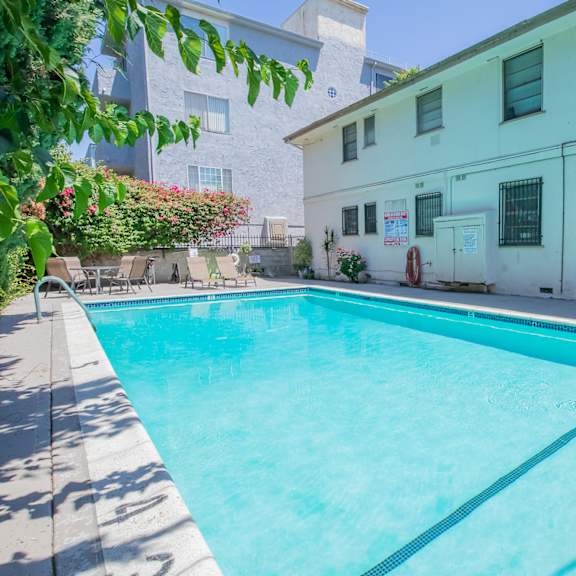 a swimming pool in front of a white building with chairs on the side