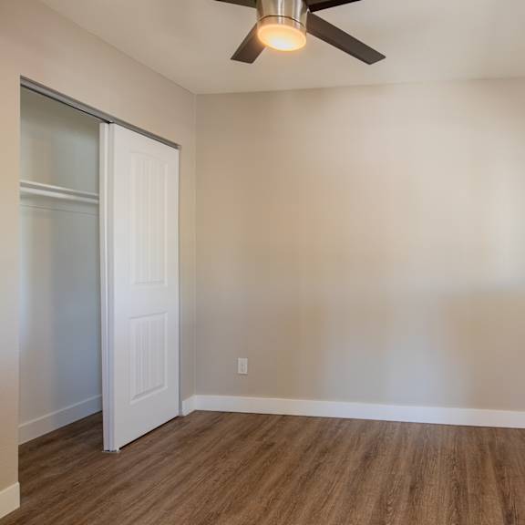 an empty bedroom with a ceiling fan and a closet