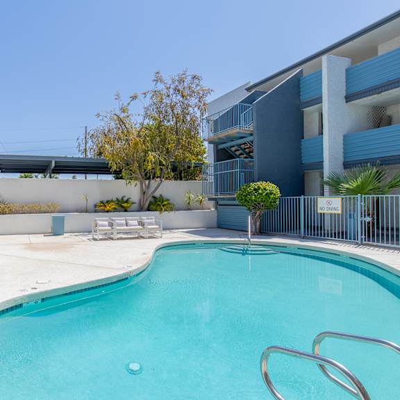a swimming pool with chaise lounge chairs and a tree in front of a blue building