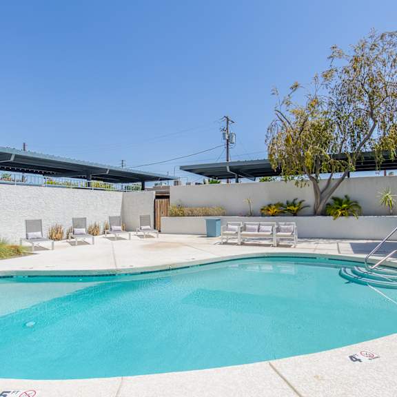 a swimming pool with lounge chairs and a tree in front of a building