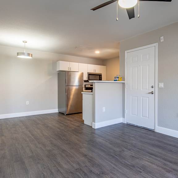 a living room with a ceiling fan and a kitchen in the background
