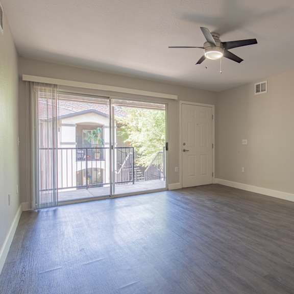 an empty living room with a sliding glass door and a ceiling fan
