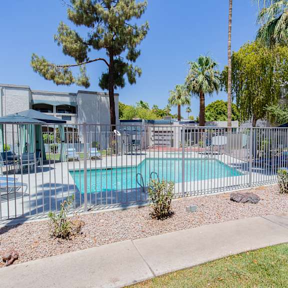 a pool surrounded by a fence and trees at sofia apartments, tempe, 85283