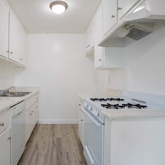 an empty kitchen with white cabinets and a stove and sink