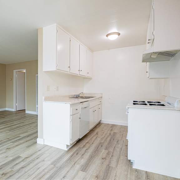 an empty kitchen and living room with white cabinets and wood floors