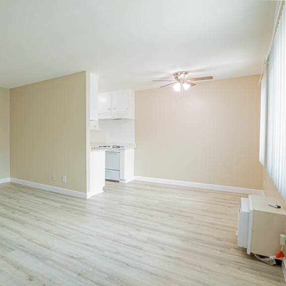 an empty living room with wood floors and a kitchen