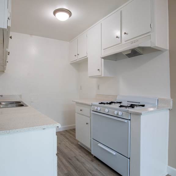 an empty kitchen with white cabinets and a stove and a sink