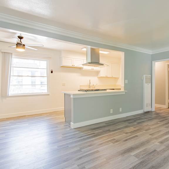 an empty living room with a kitchen and a window