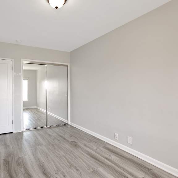 a bedroom with white walls and wood flooring and a door to a hallway