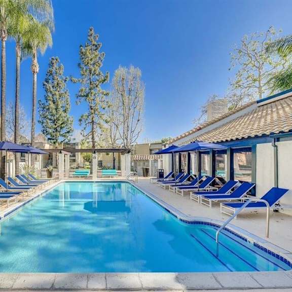 a swimming pool with blue lounge chairs and umbrellas