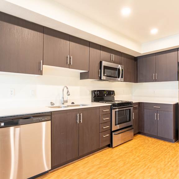 an empty kitchen with stainless steel appliances and wooden floors