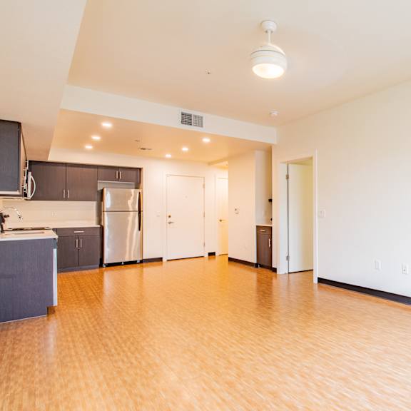 an empty living room with wood flooring and a kitchen