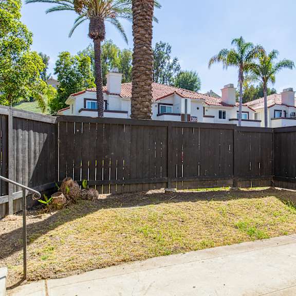 a fenced in yard with palm trees and a house in the background