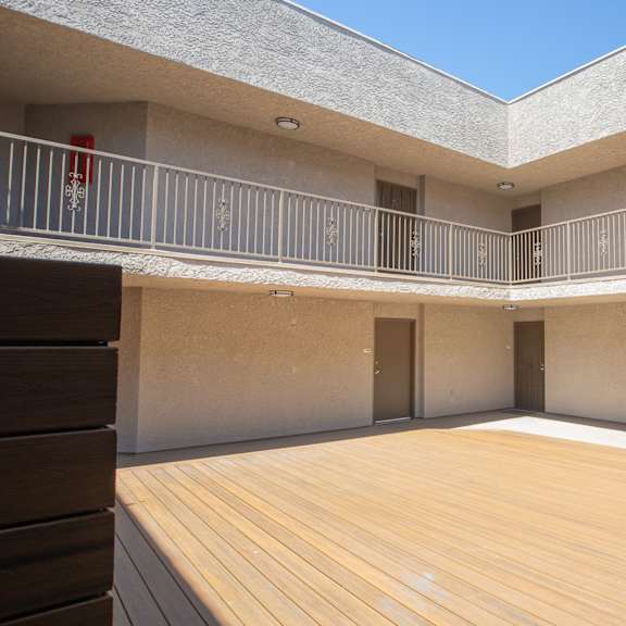 a balcony with a railing and a fire extinguisher is on the left side of a building with a wooden deck in the center.