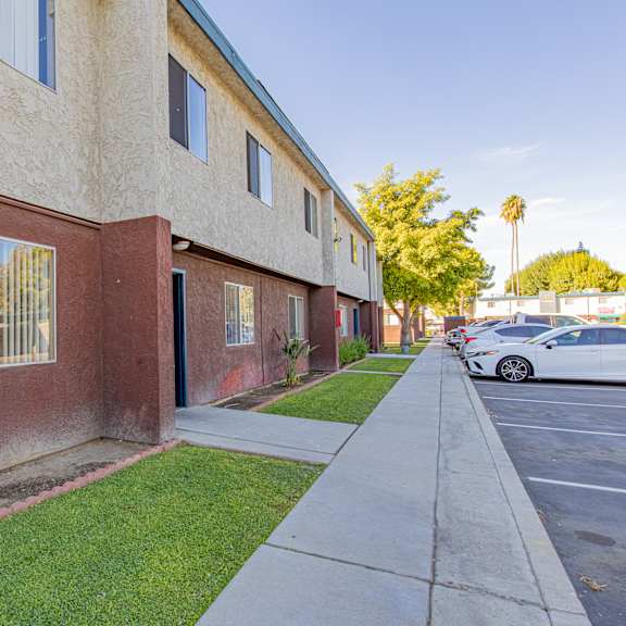 a side view of a building with a sidewalk and cars parked