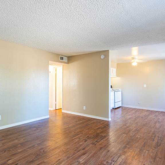 an empty living room with wood flooring and a kitchen