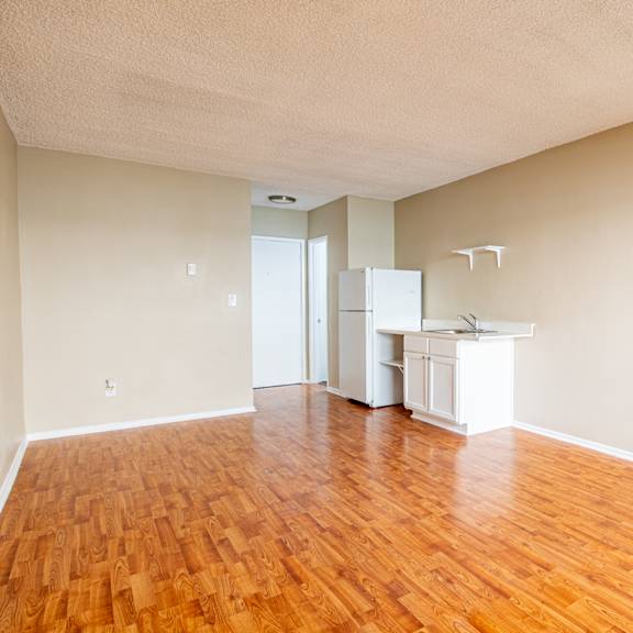 an empty living room with wood floors and a kitchen
