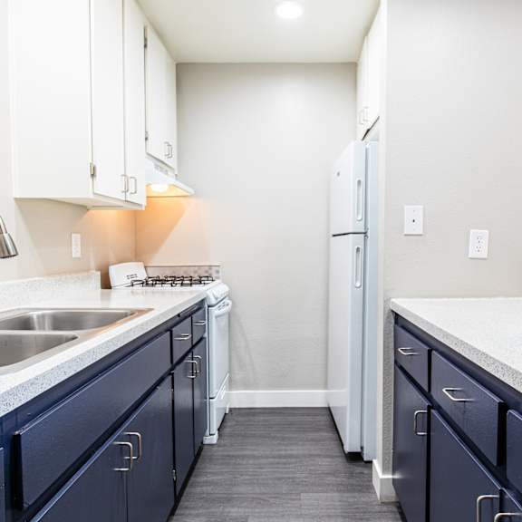 an empty kitchen with blue cabinets and a sink and a refrigerator