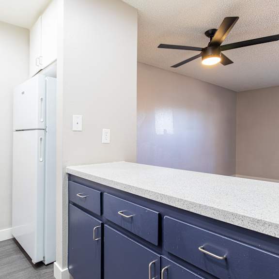 a kitchen with blue cabinets and a white refrigerator and a ceiling fan