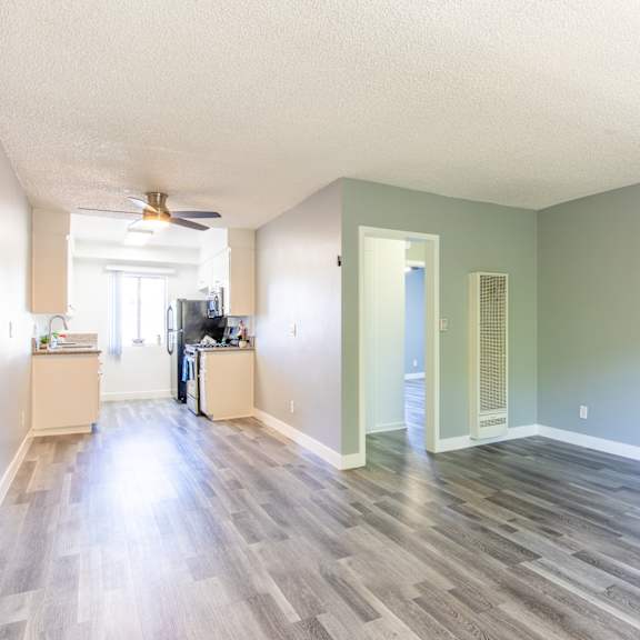 an empty living room and kitchen with wood floors and a ceiling fan