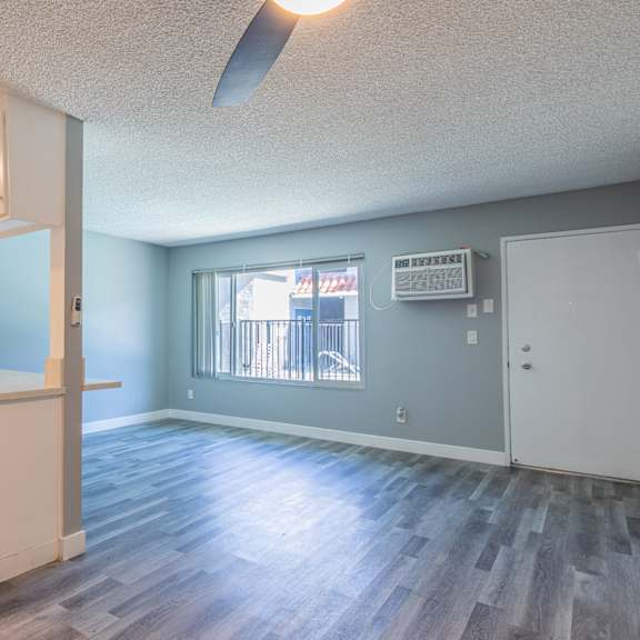 an empty living room with a kitchen and a window
