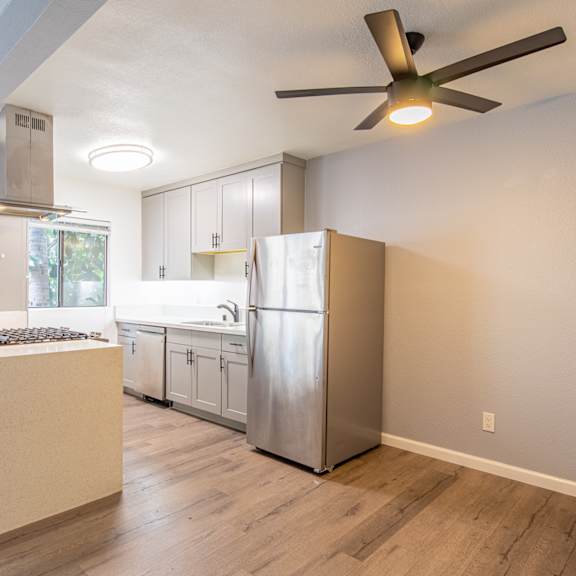 an empty kitchen with a stainless steel refrigerator and a ceiling fan