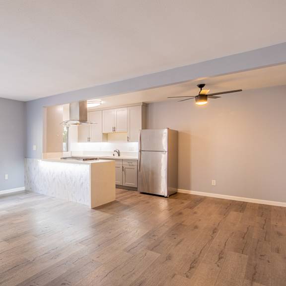 an empty living room with a kitchen and a large window