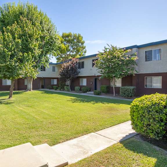 an apartment building with a lawn and trees in front of it