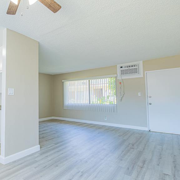 an empty living room and kitchen with white cabinets and wood floors