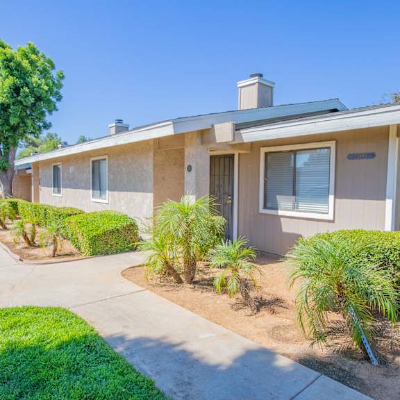 a beige house with a sidewalk and palm trees in front of it