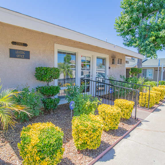 a building with a sidewalk and landscaping with plants and trees